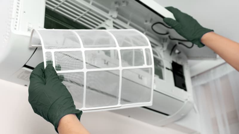 Gloved technician removing the front filter of a wall-mounted aircon unit for dust removal and cleaning